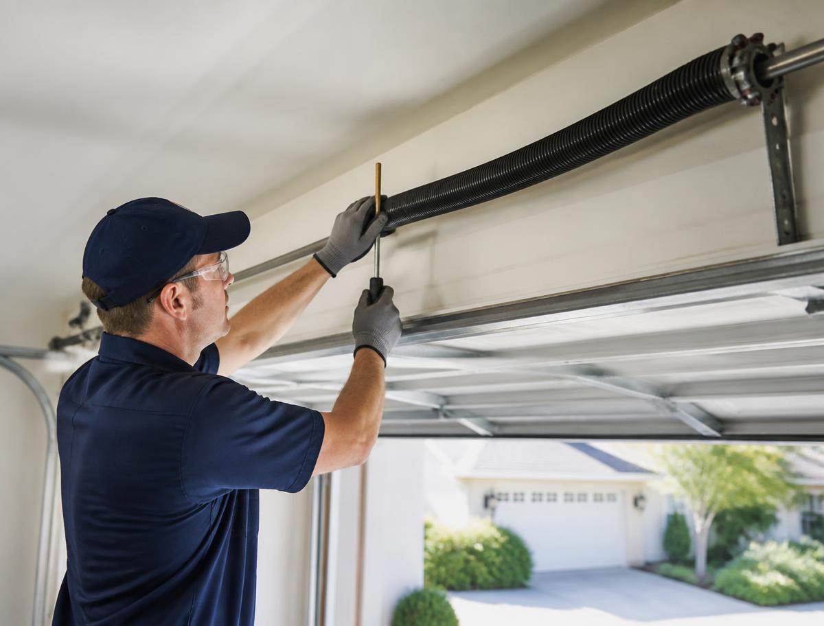 Technician winding a replacement torsion spring above a garage door